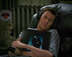 a man laying in a chair with headphones on and holding a batman poster over his face