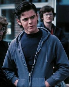 three young men standing next to each other in front of a building with one man looking at the camera