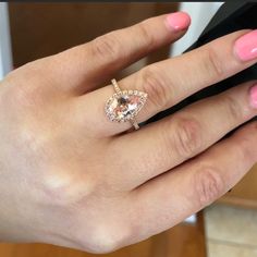 a woman's hand with a pink manicured nail polish holding an engagement ring