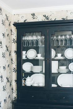 a black china cabinet with glass doors and dishes on it's sides, in front of a wallpapered wall