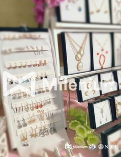 there are many necklaces and earrings on display at the table with flowers in the background