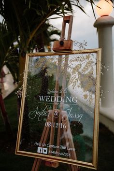 an easel with a wedding sign on it sitting in front of a palm tree