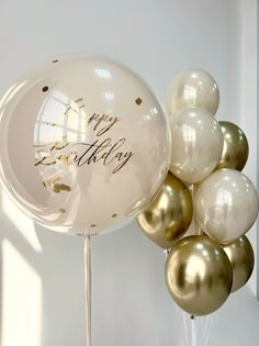 a bunch of white and gold balloons with happy birthday written on them in front of a white wall