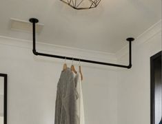 clothes hanging on rail in white room with black pipe and round light fixture over bed