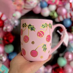 a hand holding a pink coffee cup with christmas decorations on it