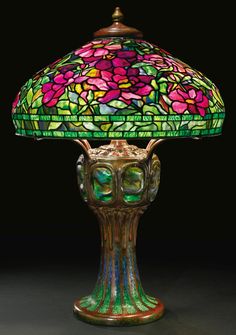 a green lamp with pink flowers on it and a red rose in the middle, sitting on a black surface