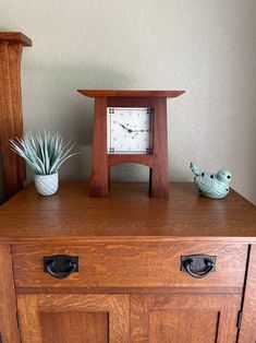 a small wooden clock sitting on top of a dresser next to a potted plant