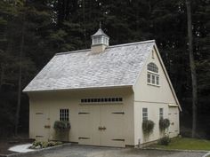 a white garage with two doors and a steeple on the roof is in front of some trees