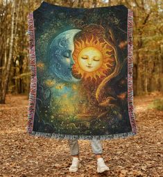 a woman standing in the woods holding up a blanket with an image of a sun and moon