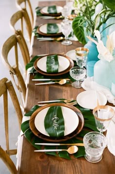 the table is set with plates, silverware and green leafy napkins on it