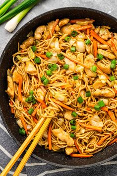 chicken lo mein with carrots and green onions in a skillet next to chopsticks