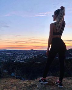 a woman standing on top of a hill looking at the city in the distance with her back to the camera