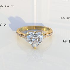 a ring with a heart shaped diamond surrounded by small diamonds on the band and in front of a white background