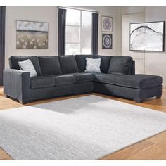 a living room with a gray sectional couch and white rug on the hardwood flooring