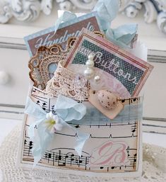 a close up of a small box on a lace doily with paper and buttons