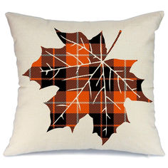 an orange and black plaid pillow with a leaf design on the front, sitting on a white background