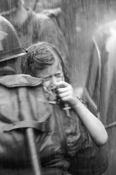 a black and white photo of a woman eating something while standing in the rain with other people behind her