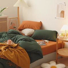 an unmade bed with green and orange comforter on it in a white room