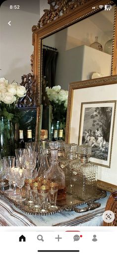 there are many wine glasses and bottles on the table next to a framed photo with flowers in it