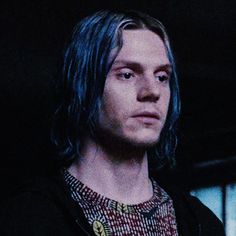 a man with long blue hair wearing a black jacket and plaid shirt is staring into the distance