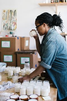 a woman standing over a table filled with lots of jars and containers full of milk