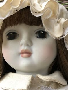 a close up of a doll wearing a white dress and hat with ruffles on it's head