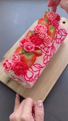 someone is decorating a strawberry cake with pink icing and flowers on it,