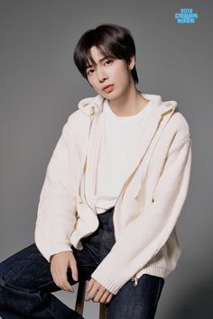 a man sitting on top of a chair wearing a white sweater and blue denim pants