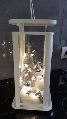 a christmas tree in a glass case with lights on the top and bottom, surrounded by snowflakes