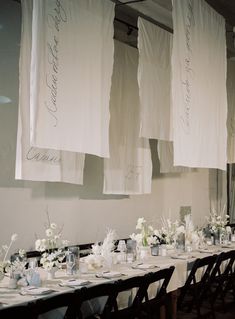 a long table is set up with white flowers and napkins hanging from the ceiling