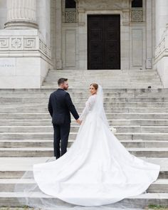 a bride and groom standing in front of the steps of an old building holding hands