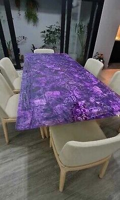 a dining room table covered in purple marble with white chairs and a fireplace behind it