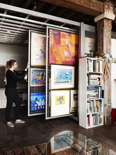 a woman standing in front of a book shelf filled with books and art on it