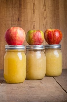 three jars filled with apples sitting on top of a wooden table next to each other