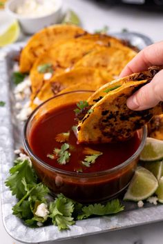 a person dipping some food into a small bowl with sauce and cilantro on the side