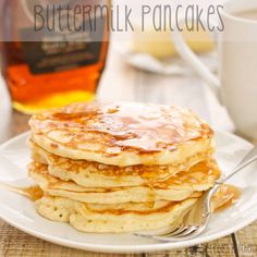 a stack of pancakes on a plate next to a cup of coffee and honey syrup