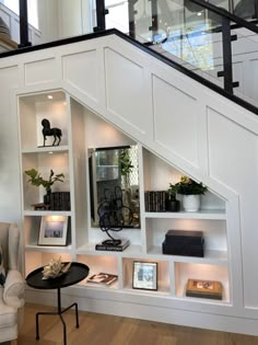 a white book shelf under a stair case with books and pictures on the shelves below