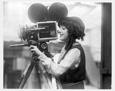 black and white photograph of a woman holding a camera with balloons in the air behind her