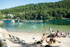 people are sitting on the beach and playing in the water at this lake while others swim