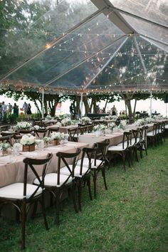 an outdoor tent with tables and chairs set up for a wedding reception under string lights