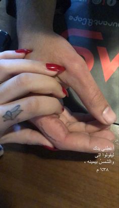 two people with red fingernails and tattoos on their fingers holding each other's hands