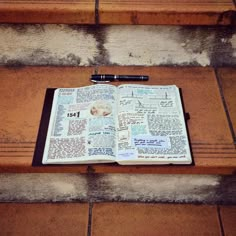 an open book sitting on top of a wooden bench next to a pen and paper