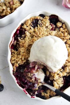 two bowls filled with blueberry crisp and ice cream on top of a white table