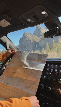 a person driving a car with a map in the passenger seat and mountains in the background