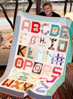 a man holding up a quilt made to look like it has letters and numbers on it