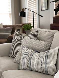 a living room filled with lots of pillows on top of a white couch next to a window