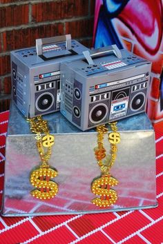 two boomboxes with chains attached to them sitting on a silver tray next to a brick wall