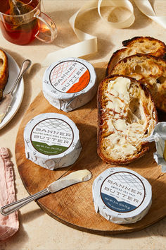 several different types of cheeses and bread on a wooden platter with spoons