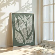 a white framed art piece sitting on top of a hard wood floor next to a window