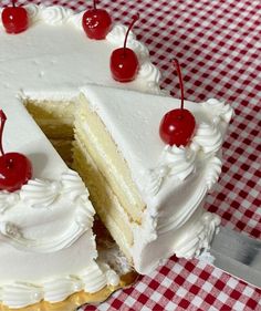 a cake with white frosting and cherries is cut in half on a checkered tablecloth